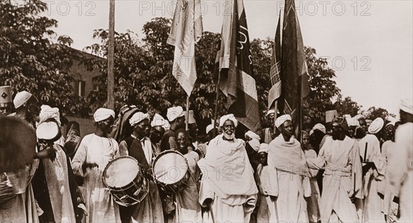Sudanese men welcome Ramadan. A group of Sudanese men, dressed in robes and turbans, bear flags and beat drums to celebrate the start of Ramadan, the ninth and holiest month of the Islamic calendar. Khartoum, Sudan, circa 1910. Khartoum, Khartoum, Sudan, Eastern Africa, Africa.