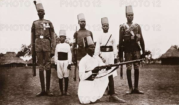 Sudanese military uniforms. Five Sudanese men and a young boy pose for the camera, wearing a variety of Egyptian Army military uniforms. All are dressed in fez hats, their uniform varying according to their station. Sudan, circa 1910. Sudan, Eastern Africa, Africa.