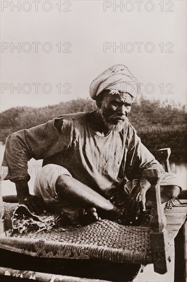 An elderly Sudanese guide. Portrait of an elderly Sudanese guide sitting cross-legged on a woven mat. Sudan, circa 1910. Sudan, Eastern Africa, Africa.