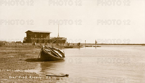 The Karachi Boat Club. A rowing boat lies on its side at China Creek in front of the Karachi Boat Club. Originally established in 1901, the social club considered boating to be a leisure pursuit rather than a serious sport. Karachi, India (Pakistan), circa 1910. Karachi, Sindh, Pakistan, Southern Asia, Asia.
