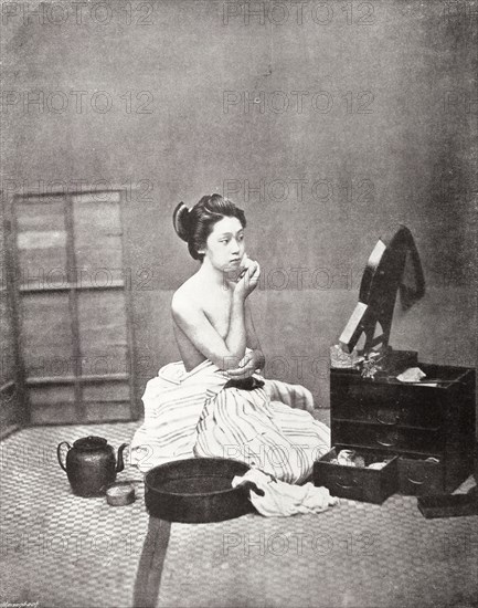 Japanese woman applying make-up. A photograph printed in 'The Sketch' newspaper features a young Japanese woman, possibly a geisha, kneeling beside her dressing table to apply make-up. Half-dressed in a kimono, she is naked from the waist up and wears her hair in traditional 'shimada' style. Japan, circa 1895. Japan, Eastern Asia, Asia.
