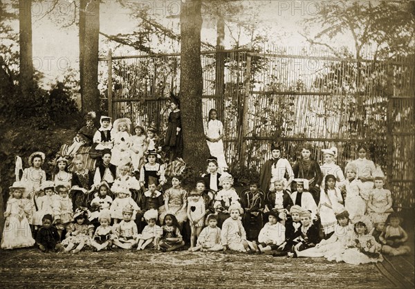 Children in historical fancy dress. A group of children pose for the camera outdoors, wearing a variety of historical fancy dress costumes, possibly for a Christmas party. Four Asian children appear amongst the group, which consists mostly of European children. Probaby India, circa 1891. India, Southern Asia, Asia.