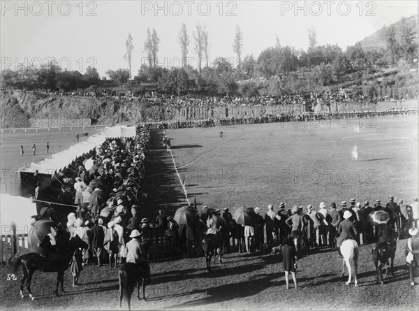 Spectators at a Durand Cup football match. An audience of mainly British spectators crowds the sidelines at a Durand Cup football match, India's oldest football tournament. More onlookers, both British and Indian, take shade beneath umbrellas as they watch the action from a hill overlooking the pitch. Simla (Shimla), India, circa 1895. Shimla, Himachal Pradesh, India, Southern Asia, Asia.