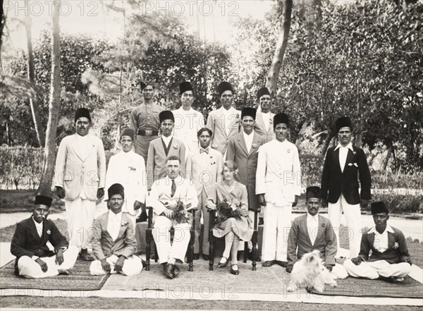 Government employees, India. A British couple, holding bouquets of flowers, pose at the centre of a group portrait with a number of Indian government workers dressed in Western-style suits and 'roomi topis' (a type of fez hat worn by Indian Muslims). The British man may be Mr Caffin, a one time District Officer of the Northern Province. India, circa 1935. India, Southern Asia, Asia.