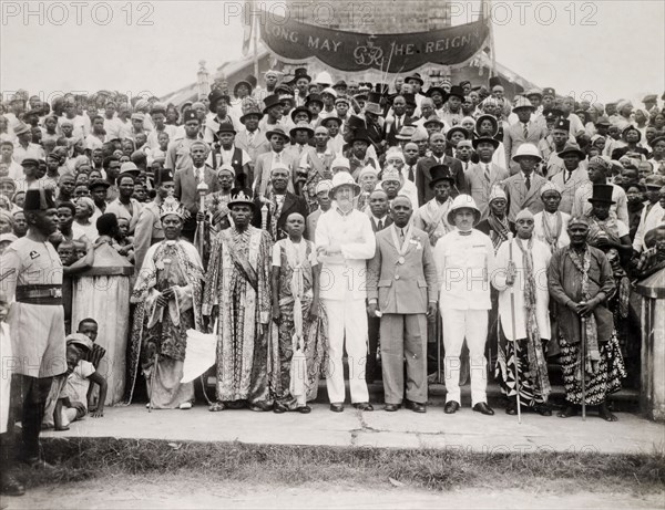 A Nigerian Native Authority Council at Calabar. Portrait of a Nigerian Native Authority Council at Calabar. A Nigerian chief and his family, dressed in ceremonial attire, stand in the front row beside three government officials (two European and one African). The large African crowd behind them wear mostly Western-style clothing, including suits, top hats and trilbies. Calabar, Cross River State, Nigeria, 1947. Calabar, Cross River, Nigeria, Western Africa, Africa.