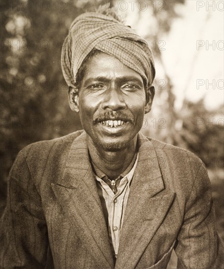 Portrait of a 'shikari'. Portrait of a smiling 'shikari' (hunter), wearing a Western-style suit and turban. Shikaris were often employed by wealthy Indian noblemen and British colonists for their knowledge of the local terrain and their traditional hunting techniques. Central India, circa 1935. India, Southern Asia, Asia.