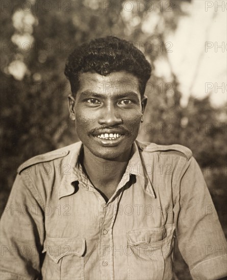 Portrait of a 'shikari'. Portrait of a smiling 'shikari' (hunter), wearing a Western-style shirt. Shikaris were often employed by wealthy Indian noblemen and British colonists for their knowledge of the local terrain and their traditional hunting techniques. Central India, circa 1935. India, Southern Asia, Asia.