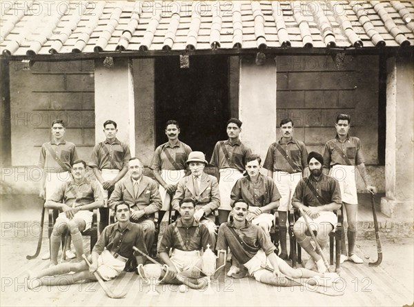 Portrait of an Indian police hockey team. Group portrait of an Indian police hockey team. Three British men pose at the centre of the group, surrounded by Indian players with their hockey sticks, who wear matching shirts and shorts. Two trophies and a hockey ball are positioned on the ground in front of them. India, circa 1940. India, Southern Asia, Asia.