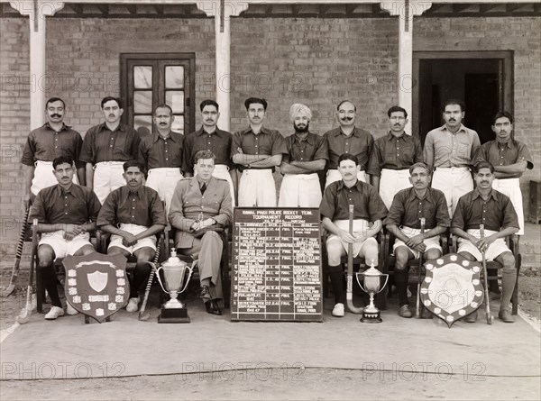 Rawalpindi Police hockey team of 1944-46. Outdoors portrait of the Rawalpindi Police hockey team with their hockey sticks and trophies. The players pose in their sports kit with the Superintendent of Police, Ray Mellor. Rawalpindi, Punjab, India (Pakistan), 1946. Rawalpindi, Punjab, Pakistan, Southern Asia, Asia.