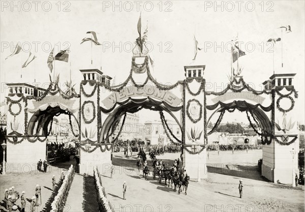 Welcome arch for the royal visit, Melbourne. A welcome arch, decorated with flags and garlands, spans a street in honour of the Duke and Duchess of Cornwall and York (later King George V and Queen Mary) who had travelled from England to open the first Commonwealth Parliament of Australia. A horse-drawn carriage passing beneath receives a military salute, suggesting its passengers are of some importance. Melbourne, Australia, May 1901. Melbourne, Victoria, Australia, Australia, Oceania.