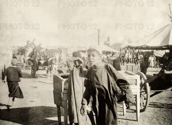 North African boys at an outdoor bazaar. Two north African boys, pictured at an outdoor bazaar. Probably Port Said, Egypt, circa 1901. Port Said, Port Said, Egypt, Northern Africa, Africa.