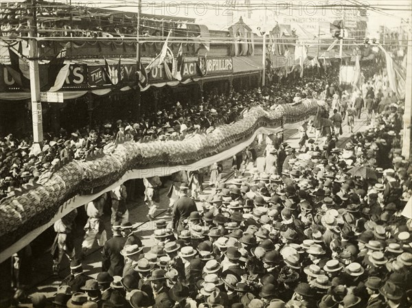 Chinese dragon dance, Perth. A Chinese dragon dance winds its way through crowds of spectators who have gathered in Perth's China Town district to welcome the Duke and Duchess of Cornwall and York (later King George V and Queen Mary) on their visit to the city. Perth, Australia, July 1901. Perth, West Australia, Australia, Australia, Oceania.