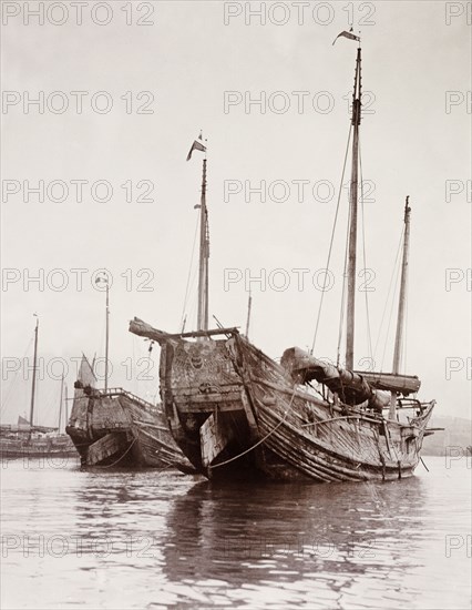 Junks moored at a Hong Kong harbour. Two Chinese junks are moored at a Hong Kong harbour with their rudders raised up out of the water. Hong Kong, China, circa 1903., Hong Kong, China, People's Republic of, Eastern Asia, Asia.