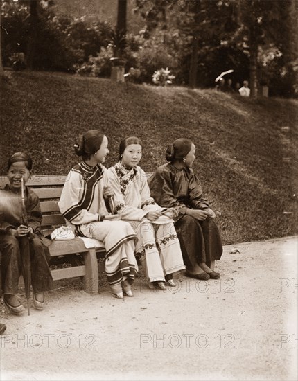 Chinese girls in a public garden in Hong Kong. Three Chinese girls, accompanied by an 'amah' (nursemaid), sit on a wooden bench in a public garden. They are dressed in traditional 'shenyi' and their hair is neatly tied up. Hong Kong, China, circa 1903. Hong Kong, Hong Kong, China, People's Republic of, Eastern Asia, Asia.