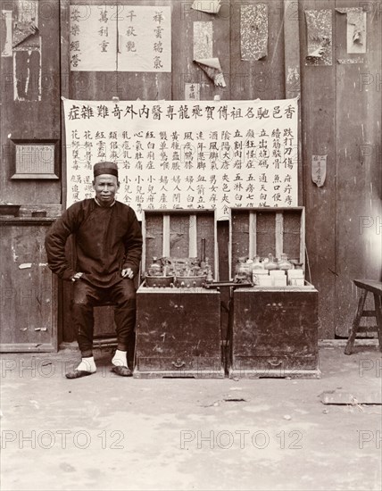 An itinerant medicine man, Hong Kong. An itenerant medicine man sits at a street stall selling various potions and remedies to passers-by. A large board inscribed with Chinese script advertises his wares. Hong Kong, China, circa 1903. Hong Kong, Hong Kong, China, People's Republic of, Eastern Asia, Asia.