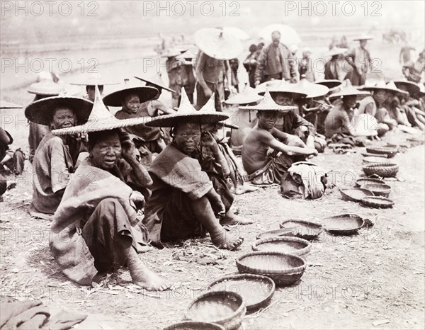 Mendicants beg by the roadside, China. A number of mendicants, some of whom are suffering from leprosy, beg at the roadside with their woven bowls. Both men and women wear wide-brimmed conical hats. Shikuan, Yunnan Province, China, circa 1905. Shikuan, Yunnan, China, People's Republic of, Eastern Asia, Asia.
