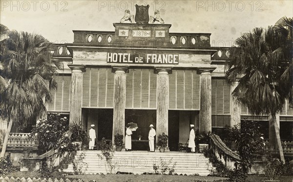 The Hotel de France in Chandannagar. The Hotel de France in Chandannagore, built in 1878 as indicated by a stone plaque above the entrance. A British couple and two Indian servants stand on the steps outside the hotel. Chandannagore, French India (Chandannagar, West Bengal, India), 16 March 1922. Chandannagar, West Bengal, India, Southern Asia, Asia.
