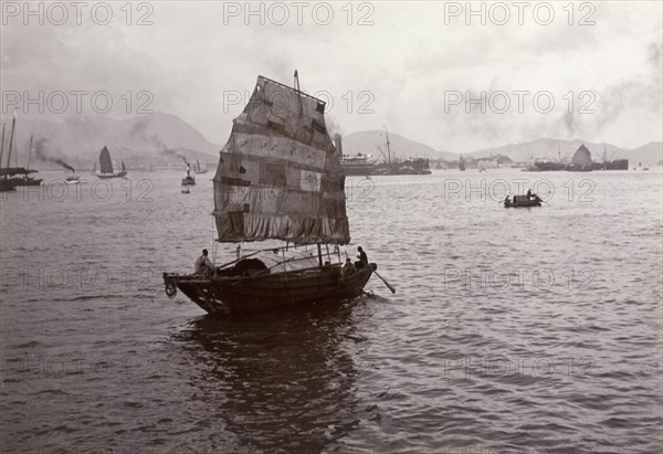 Sampan with a patchwork sail. A Chinese sampan, fitted with a distinctive patchwork sail, sails in the calm waters of Victoria Harbour. Hong Kong, China, circa 1903. Hong Kong, Hong Kong, China, People's Republic of, Eastern Asia, Asia.
