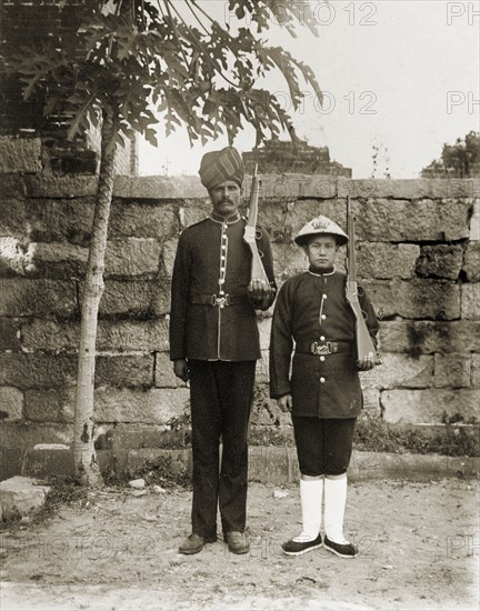 Indian and Chinese officers of the Hong Kong Police Force. Two Hong Kong police officers, one Indian and one Chinese, stand to attention, side-by-side, with their rifles over their shoulders. Police uniform varied according to ethnicity: the Indian officers wore turbans, whilst the Chinese officers wore conical straw hats. Hong Kong, China, circa 1903. Hong Kong, Hong Kong, China, People's Republic of, Eastern Asia, Asia.