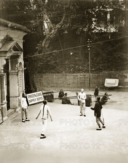 Playing football with a shuttlecock. Four young Chinese men play football with a shuttlecock outside the Dairy Farm office and frozen food depot. Their hair is worn in 'queues' (waist-long pigtails), in traditional Manchu style. Hong Kong, China, circa 1905. Hong Kong, Hong Kong, China, People's Republic of, Eastern Asia, Asia.