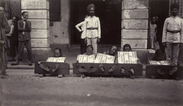 Petty criminals in the stocks, Hong Kong. A group of petty criminals sit with their ankles restrained in stocks, guarded by a pair Indian officers from the Hong Kong Police Force. Each wears a board strung around the neck, describing in detail the offense committed. Hong Kong, China, circa 1905. Hong Kong, Hong Kong, China, People's Republic of, Eastern Asia, Asia.
