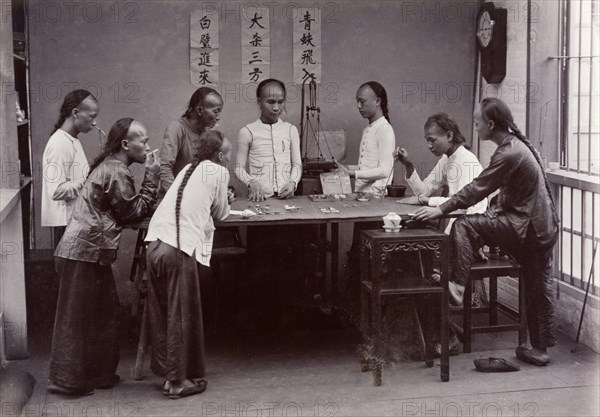 Chinese gambling game of 'fantan'. Eight men with distinctive Manchu hairstyles gather around a table to play the traditional Chinese gambling game of 'fantan'. Hong Kong, China, circa 1905. Hong Kong, Hong Kong, China, People's Republic of, Eastern Asia, Asia.