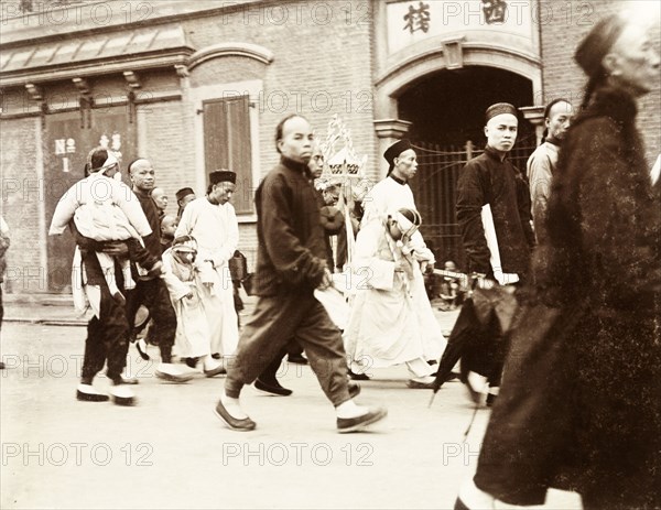 A wealthy Chinese funeral procession. Mourners at a wealthy Chinese funeral procession follow a coffin along a city street. Traditionally, the closest family members to the deceased wore black, whilst more distant relations wore lighter colours or white. Children's heads would often be covered with sackcloth hoods as a sign of respect. China, circa 1905. China, People's Republic of, Eastern Asia, Asia.