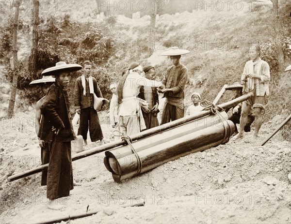 A working-class Chinese funeral. A group of mourners, including one paid mourner dressed in white, gather for the burial of a working-class person. A simple coffin, constructed from four lengths of timber bound together, lies on the ground beside a freshly dug grave. China, circa 1905. China, People's Republic of, Eastern Asia, Asia.