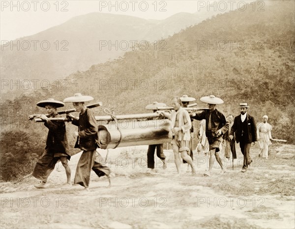 A working-class Chinese funeral procession. Four pallbearers carry the simply-constructed coffin of a working-class person to a rural burial site. A group of mourners follow behind, including one European man dressed in Western-style clothing. China, circa 1905. China, People's Republic of, Eastern Asia, Asia.