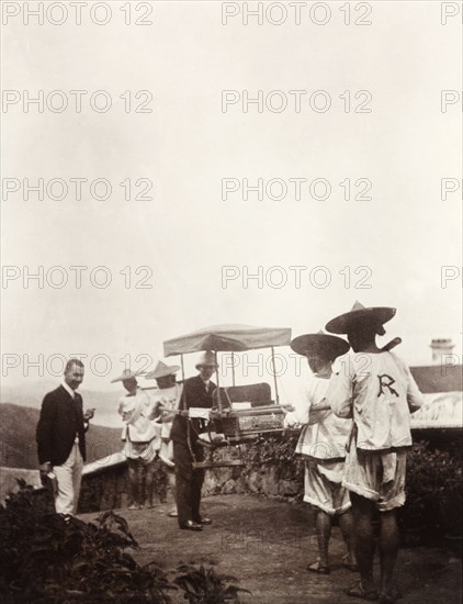 Two doctors with a sedan chair. Two British doctors, Dr Rennie (left) and Dr Marriott (right), stand beside a sedan chair carried by Chinese servants. Probably Hong Kong, China, circa 1905., Hong Kong, China, People's Republic of, Eastern Asia, Asia.