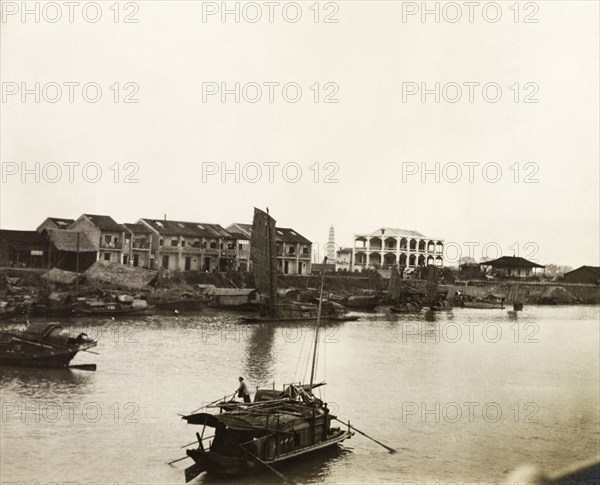 Boats on the Xijiang River at Sam Shui. A sampan travels along the Xijiang River at Sam Shui, passing a string of boats moored along the riverbank. Sam Shui, Canton Province (Sanshui, Guangdong), China, circa 1906. Sanshui, Guangdong, China, People's Republic of, Eastern Asia, Asia.