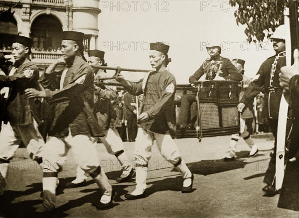 The Duke of Connaught visits Hong Kong, 1906. A team of Chinese bearers, wearing a uniform of scarlet coats and velvet hats, carry the Duke of Connaught through the streets of Hong Kong in a sedan chair. The Duke made his visit shortly before a devastating typhoon struck the city on 18 September. Hong Kong, China, August 1906. Hong Kong, Hong Kong, China, People's Republic of, Eastern Asia, Asia.