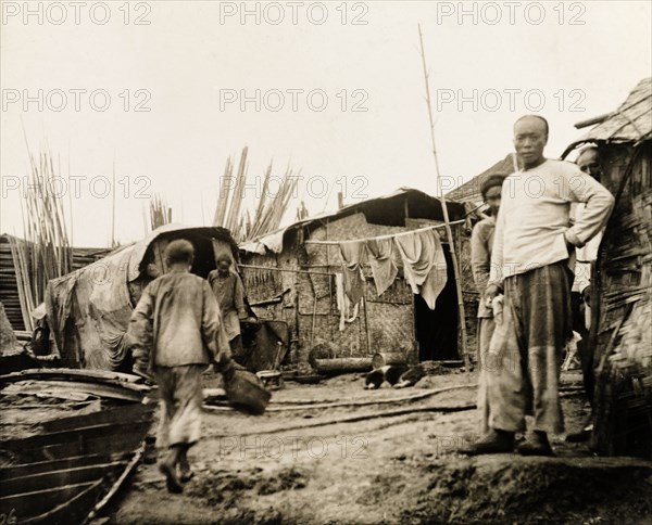 Settlement on the banks of the Yangtze River. People mill about at a settlement containing several woven bamboo dwellings with canvas roofs on the banks of the Yangtze River. China, circa 1910. China, People's Republic of, Eastern Asia, Asia.