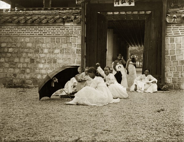 Korean women in traditional 'hanbok' dress. A group of Korean women and girls sit in the grounds of an imperial palace in Seoul. All wear traditional 'hanbok' dress, comprising full-length skirts and wide-sleeved, hip-length jackets or shirts. Seoul, Korea (South Korea), circa 1920 Seoul, Special City, South Korea, Eastern Asia, Asia.