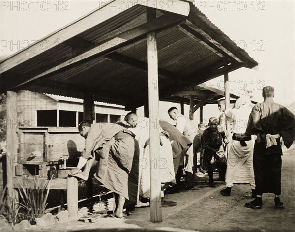 Freshening up at railway station in Manchuria. A group of Japanese travellers refresh themselves at a railway station in southern Manchuria, washing their feet in a series of wooden sinks equipped with running water. China, circa 1920. China, People's Republic of, Eastern Asia, Asia.