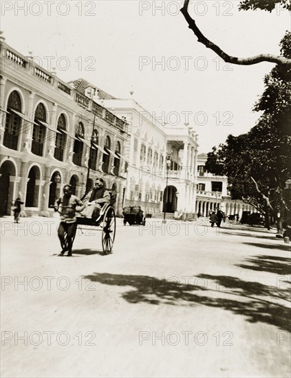 Rickshaw on the 'praya' in Macao. A rickshaw travels along the 'praya' (waterfront promenade) in Macao, flanked on one side by several multi-storey colonial buildings. Macao (Macau), China, circa 1920. Macau, Macau, China, People's Republic of, Eastern Asia, Asia.