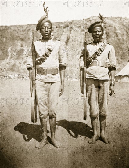 Armed Zulu policemen. Two armed Zulu policemen stand to attention, wearing feathered berets and bandoliers. Embabaan (Mbabane), Swaziland, circa August 1904. Mbabane, Hhohho, Swaziland, Southern Africa, Africa.