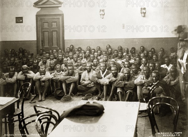 A Matabele indaba with Captain Lawley. Matabele indunas (chiefs) sit on the floor of the Stock Exchange Hall with their arms wrapped around their knees. The group were attending an indaba (council) headed by Captain Arthur Lawley, Administrator of Matabeleland and Mashonaland, and the Chief Native Commissioner to discuss arrangements for administering Matabeleland. Bulawayo, Rhodesia (Zimbabwe), 1897. Bulawayo, Matabeleland North, Zimbabwe, Southern Africa, Africa.