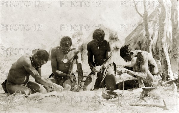 Tanners preparing a hide. Four tanners work on an animal hide that has been pegged to the ground, equipped with metal scrapers to remove hair from the skin. Rhodesia (Zimbabwe), circa 1897. Zimbabwe, Southern Africa, Africa.