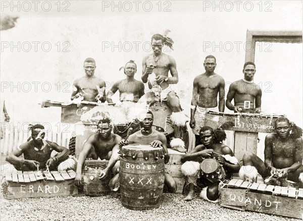 A Zulu percussion band. Group portrait of a Zulu percussion band posing by their drums and xylophones made from packing cases. Names are painted on the instruments, such as 'Erard', 'Boosey', and 'Quandt'. The men wear animal hair garters below the knees and around the ankles, similar to those worn by Zulu warriors. Kimberley, South Africa, circa 1897. South Africa, Southern Africa, Africa.
