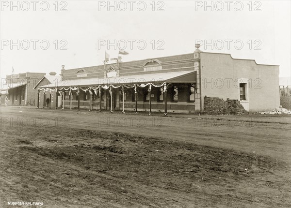 Street decorations on 'White's Building'. A colonial-style commercial building identified as 'White's Building', is decorated with flags and banners with a sign that reads: 'Welcome to Rhodesia'. Rhodesia (Zimbabwe), circa 1898. Zimbabwe, Southern Africa, Africa.