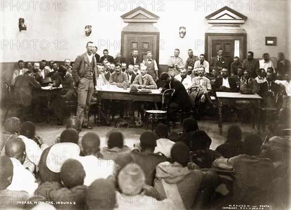 A Matabele indaba with Captain Lawley. British colonial officer, Mr W. Thomas, addresses an audience of Matabele indunas (chiefs), who are seated on the floor of the Stock Exchange Hall. They were attending an indaba (council) headed by Captain Arthur Lawley, Administrator of Matabeleland and Mashonaland, and the Chief Native Commissioner to discuss arrangements for administering Matabeleland. Bulawayo, Rhodesia (Zimbabwe), 1897. Bulawayo, Matabeleland North, Zimbabwe, Southern Africa, Africa.