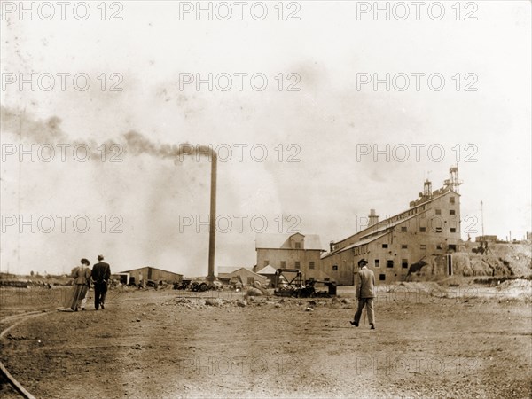 De Beers diamond mine in Kimberley. A tall, smoking chimney stands beside a factory building at the De Beers diamond mine in Kimberley. Kimberley, South Africa, circa 1896. Kimberley, North Cape, South Africa, Southern Africa, Africa.