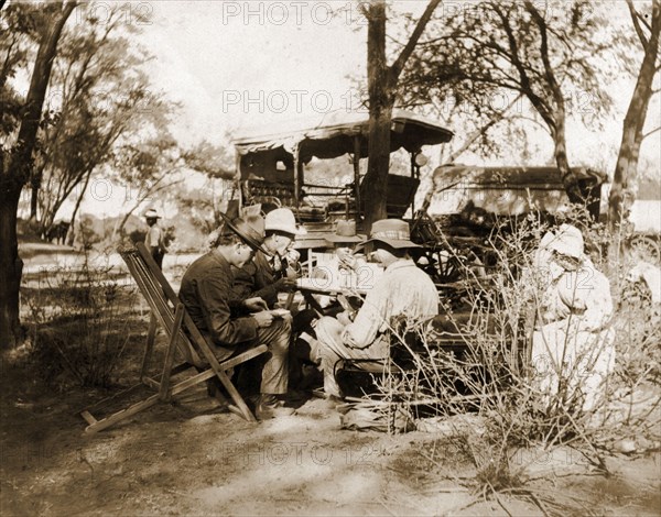 Captain Lawley stops for lunch. Captain Arthur Lawley (1860-1932) (front right) takes lunch with fellow European travellers during an overland journey from South Africa to Rhodesia. Accompanied by Earl Grey (1851-1917), he was travelling with relief forces and supplies to Bulawayo, which had been besieged during the Matabele rebellion. Probably Bechuanaland (Botswana), circa March 1896. Botswana, Southern Africa, Africa.