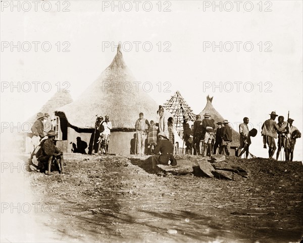 Matabele men at Cecil Rhodes' farm. Matabele (Ndebele) men mill about beside a cluster of thatched huts at Cecil Rhodes' farm in Sauerdale. Rhodes bought the farm after negotiating an end to the Matabele rebellion, and settled some Matabele people there in part fulfilment of a promise to provide them with decent land. Near Bulawayo, Rhodesia (Matabeleland North, Zimbabwe), circa 1897., Matabeleland North, Zimbabwe, Southern Africa, Africa.