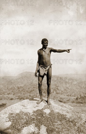 Matabele guide at the Matopos Hills. A Matabele (Ndebele) guide stands on the top of a granite boulder in the Matopos Hills, pointing out into the distance. He was accompanying a party of colonial officers including Cecil Rhodes, who was later buried in these hills. Near Bulawayo, Rhodesia (Zimbabwe), circa 1897. Bulawayo, Matabeleland North, Zimbabwe, Southern Africa, Africa.