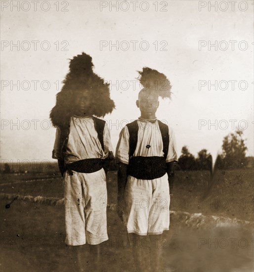 State footmen' at Government House. Outdoors portrait of two 'state footmen' at Government House in Bulawayo. The young men stand side-by-side, dressed in matching uniforms comprising elaborately feathered headdresses, waistcoats and cummerbunds. Bulawayo, Rhodesia (Zimbabwe), circa 1897. Bulawayo, Matabeleland North, Zimbabwe, Southern Africa, Africa.