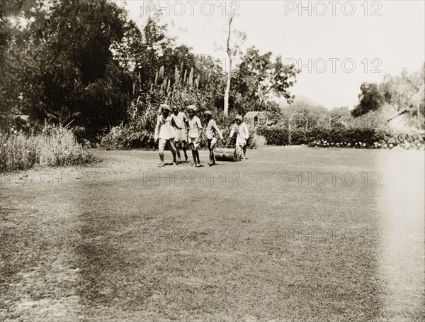 Indian servants gardening. Four Indian servants pull a roller over a tidy lawn, while a fifth man steers it from behind. Ajmer, Ajmer-Merwara (Rajasthan), India, circa 1927. Ajmer, Rajasthan, India, Southern Asia, Asia.