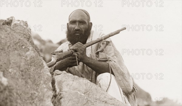 Portrait of an armed Afridi man. Portrait of an armed Afridi man, crouched behind a rock at Kohat Pass. Kohat, North West Frontier Province, India (Pakistan), circa 1925. Kohat, North West Frontier Province, Pakistan, Southern Asia, Asia.