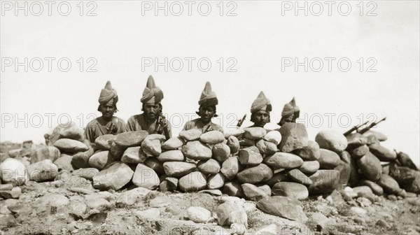 Five frontier guards. Five armed guards, dressed in uniforms and turbans, peer over the top of a dry stone wall with their guns positioned in front of them. An original caption labels them as both 'Frontier Constabulary' officers and 'Khassadars'. Although both organisations recruited local men to police the frontier, their setup and administration remained quite different. North West Frontier Province, India (Pakistan), circa 1927., North West Frontier Province, Pakistan, Southern Asia, Asia.